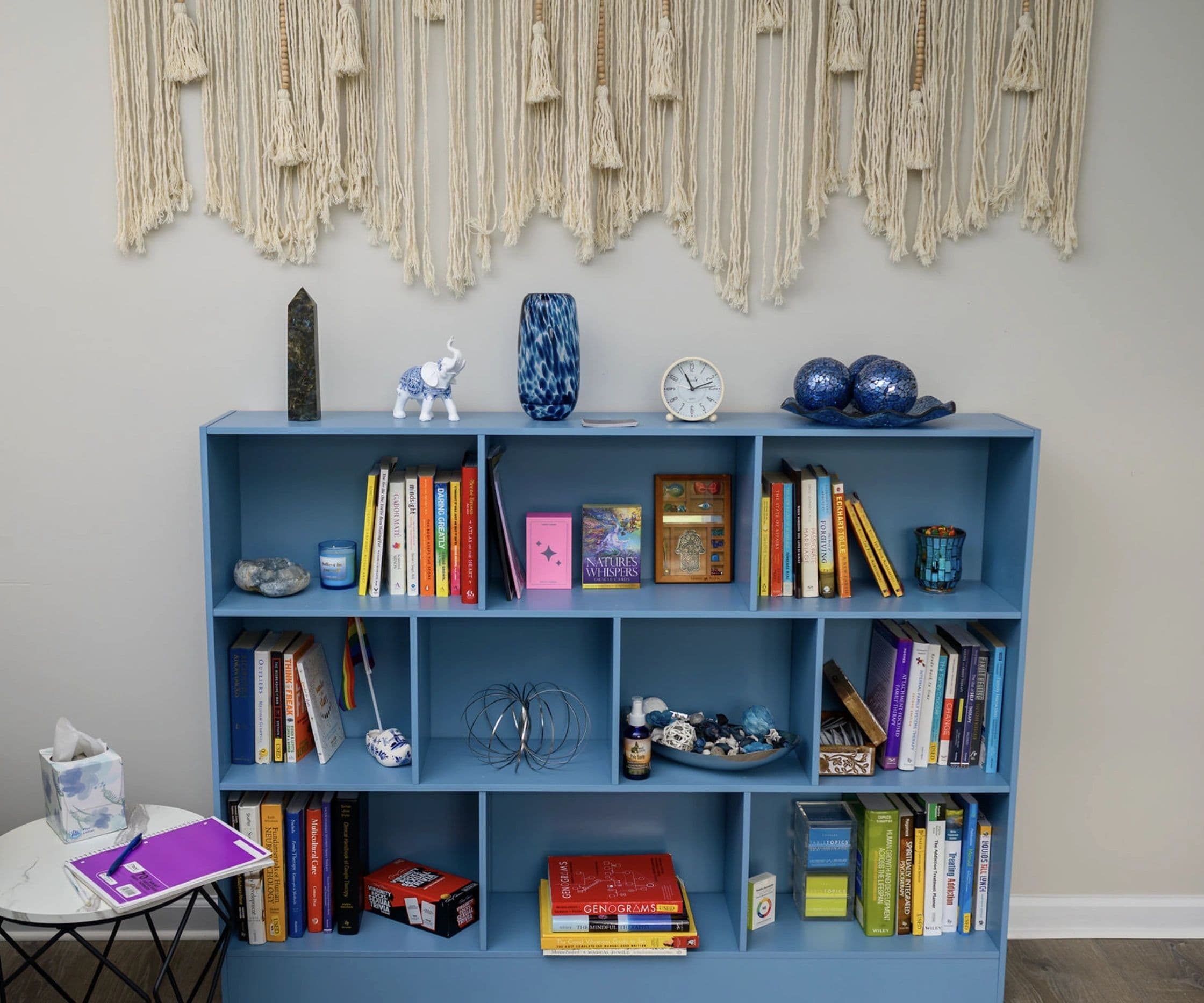 A bookshelf in Gabbie's office, filled with therapy books, oracle cards, crystals, and a small pride flag